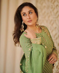 Woman in a green traditional outfit with gold details against a beige wall.