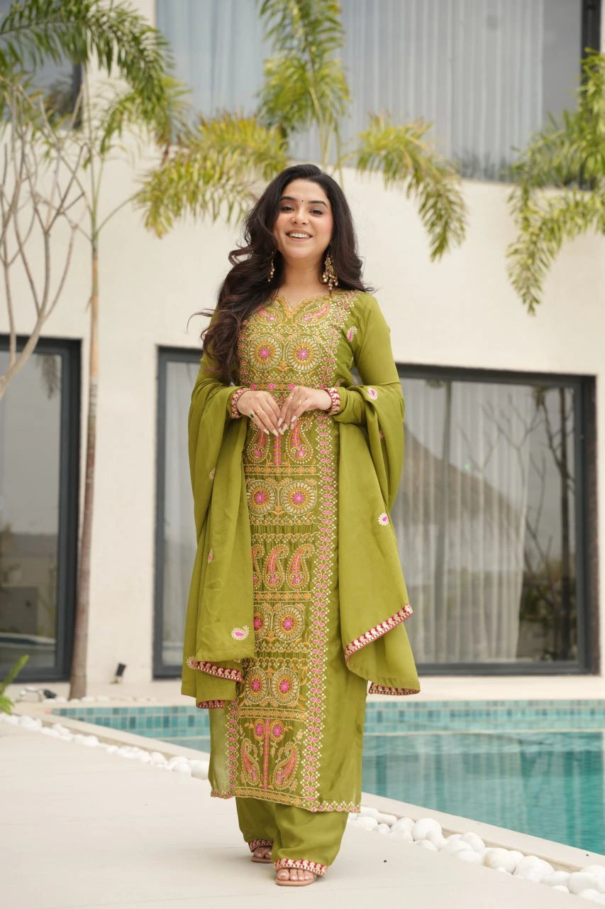 Woman in a green embroidered traditional outfit standing by a pool with greenery in the background