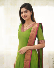 Woman wearing a green saree with a pink border on a light background
