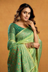 Woman wearing a green saree with a gold border on a beige background
