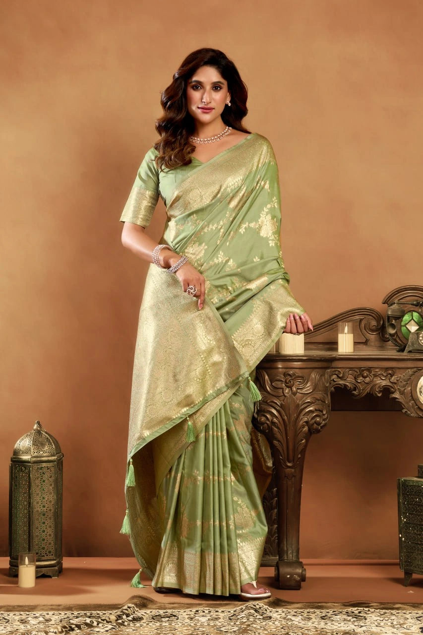 Woman in a light green saree standing next to a wooden table with decorative items on a brown background