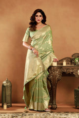 Woman in a light green saree standing next to a wooden table with decorative items on a brown background