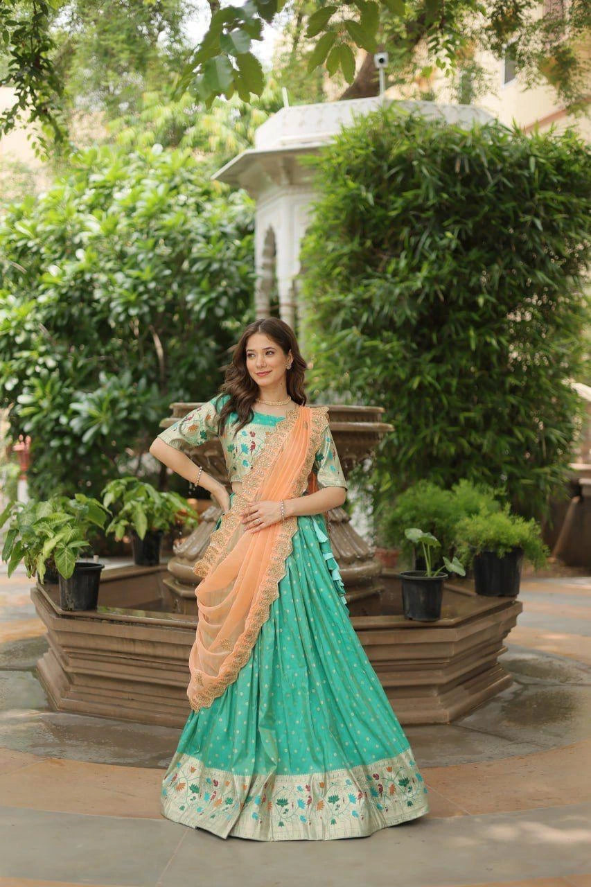 Woman in a green and peach saree standing outdoors with greenery around