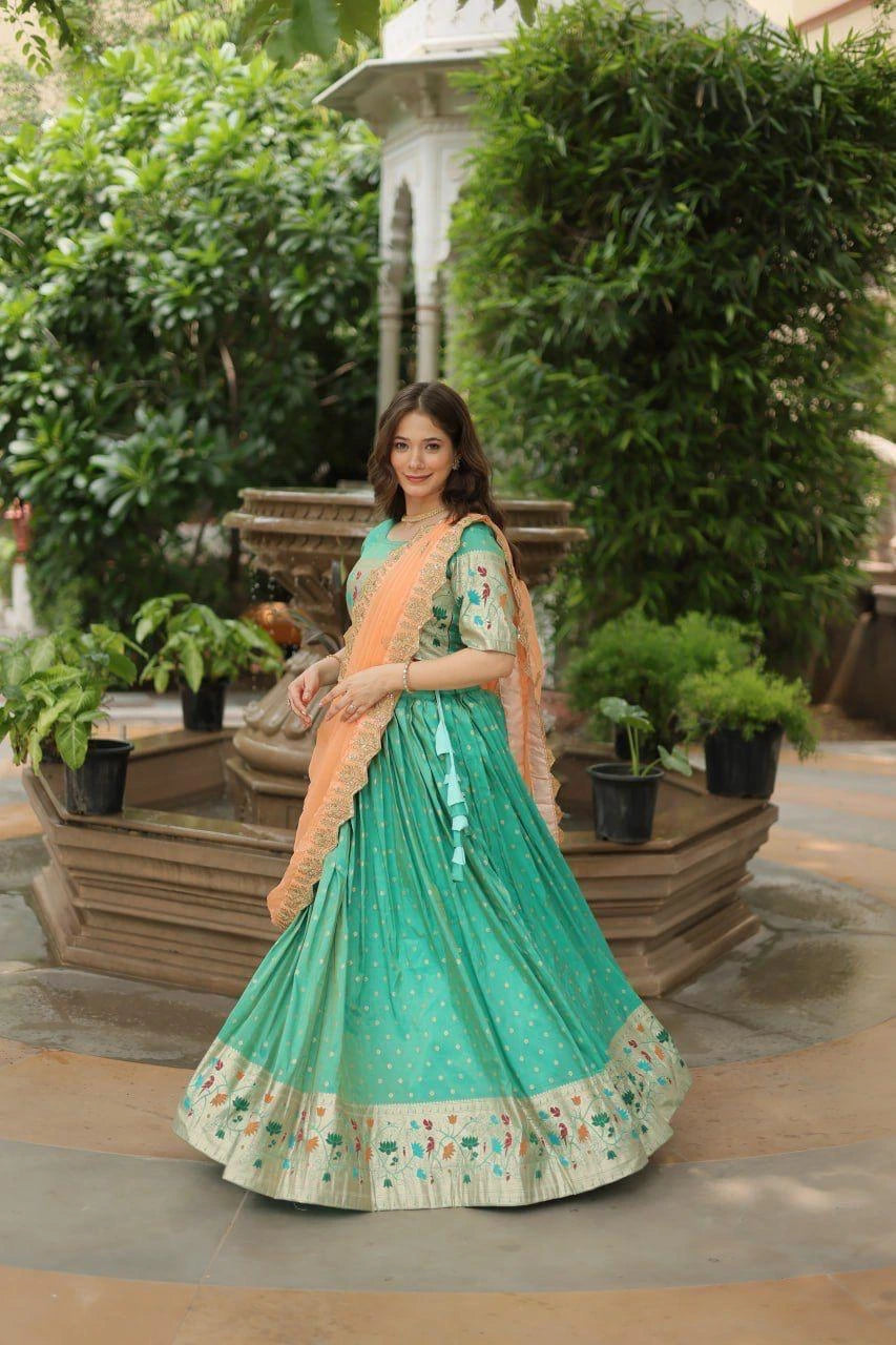 Woman in a green and peach traditional outfit standing outdoors with greenery.