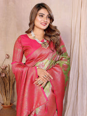 Woman wearing a pink saree with a green border, sitting against a beige curtain.