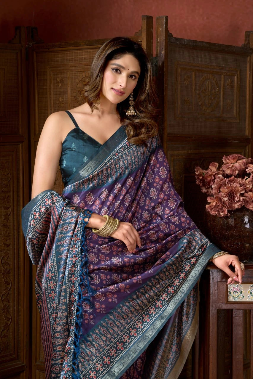 Woman wearing a blue and purple saree with floral patterns in an indoor setting.
