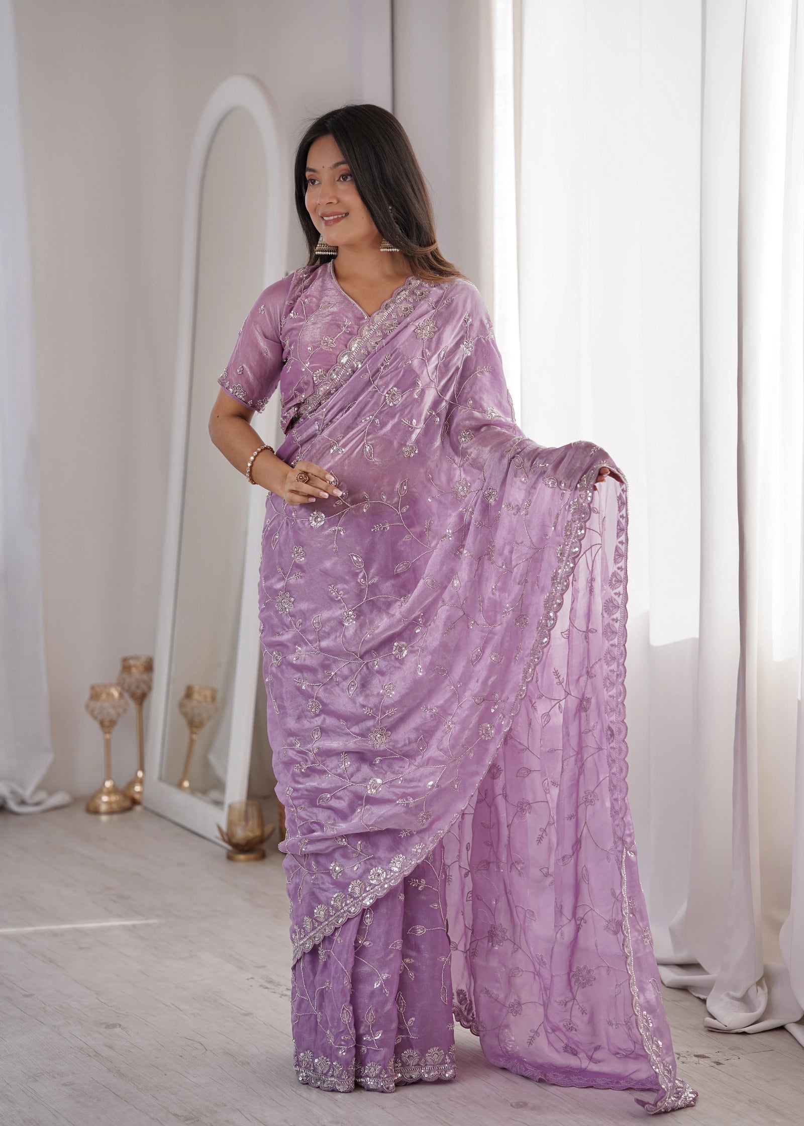 Woman wearing a purple saree with silver embroidery in a well-lit room.