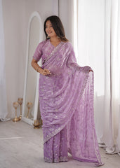 Woman wearing a purple saree with silver embroidery in a well-lit room.