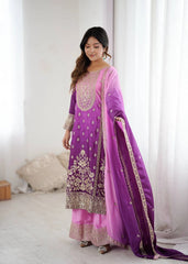 Woman wearing a purple and pink traditional outfit with intricate designs in a bright room.