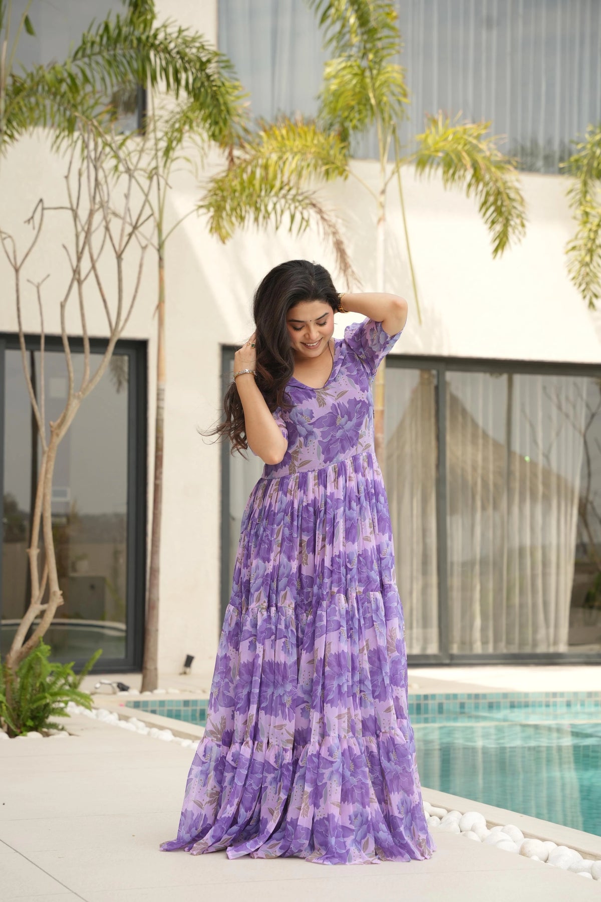 Woman in a purple dress standing by a pool with a building and trees in the background