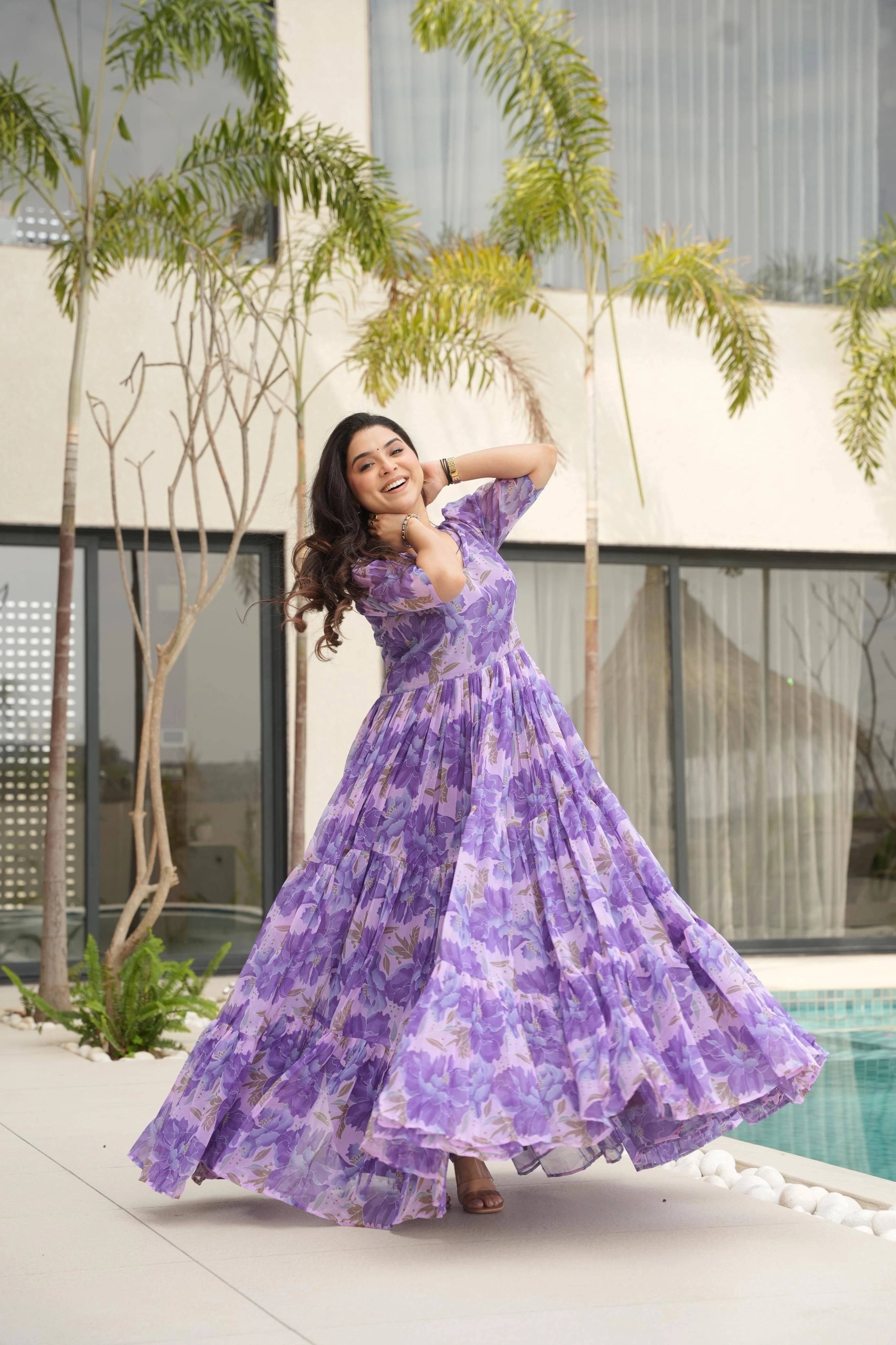 Woman in a purple floral dress posing outdoors near a pool