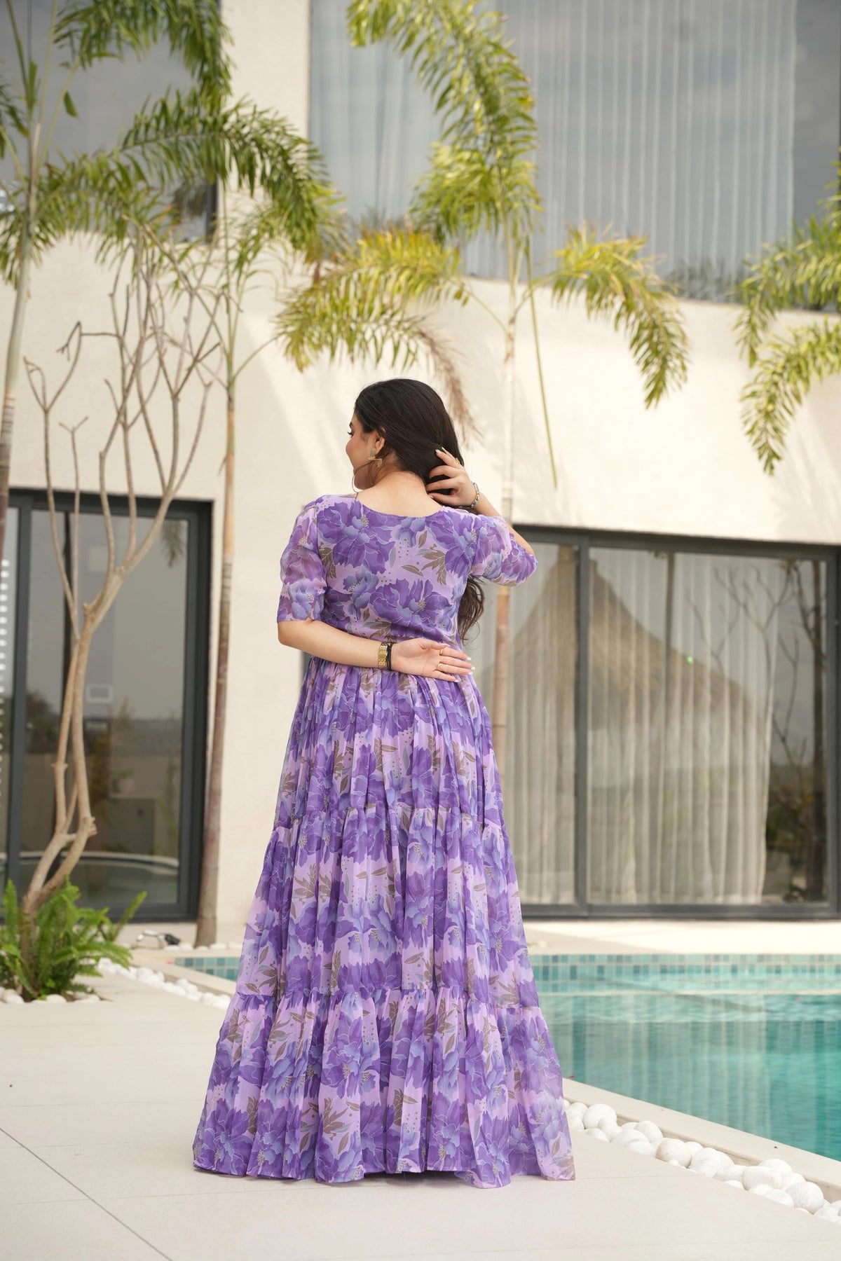 Woman in a purple dress standing by a pool with a modern building and trees in the background