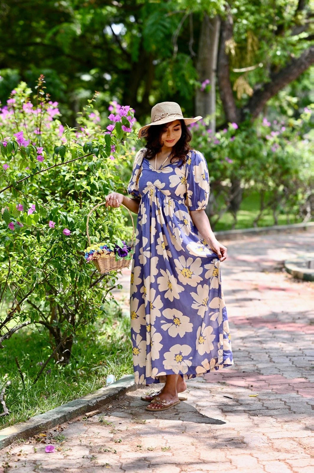 Woman in a floral dress walking on a path with greenery and flowers around.