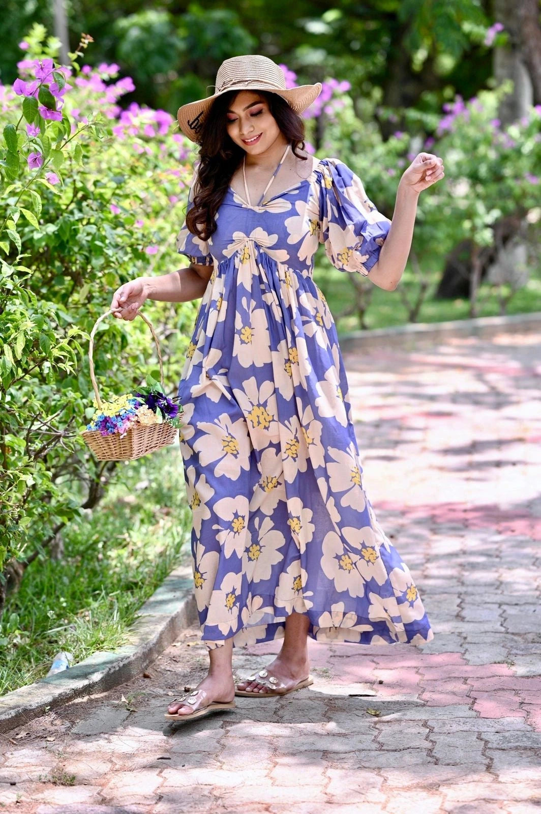 Woman in a floral dress and hat standing on a path with flowers around