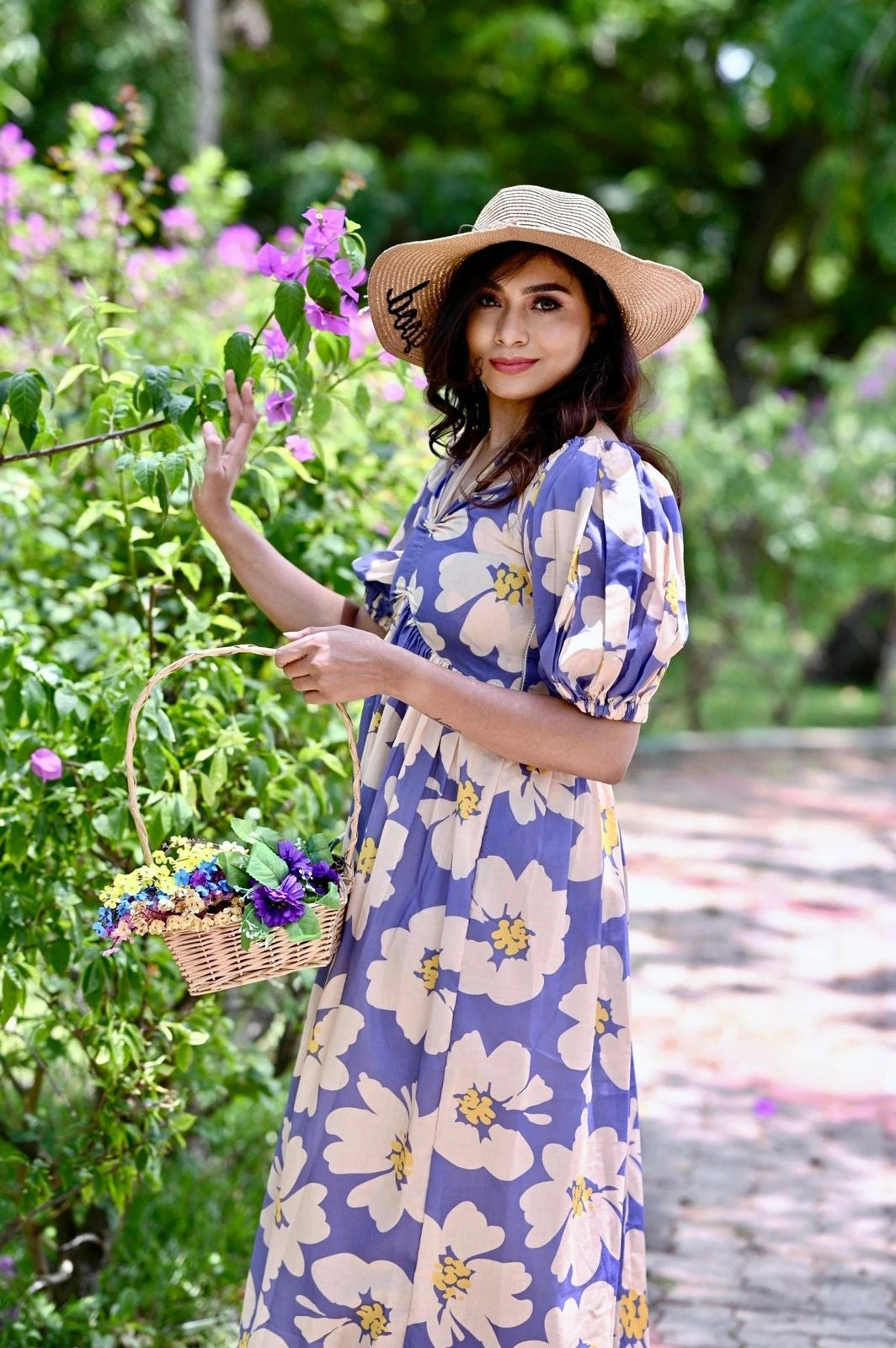 Woman in a floral dress and hat holding a basket in a garden