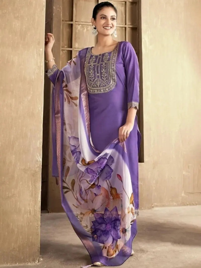 Woman wearing a purple traditional outfit with a floral scarf against a beige wall.