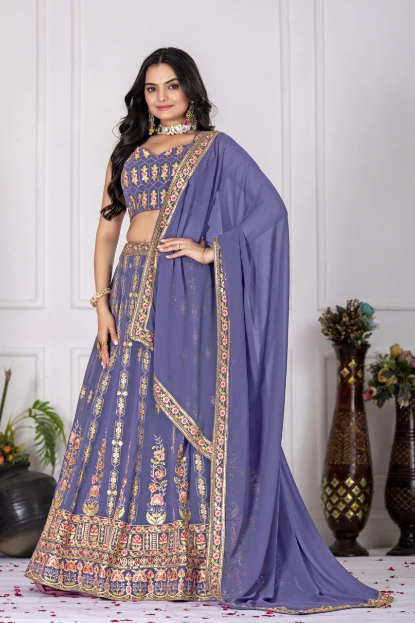 Woman wearing a traditional purple saree with gold embroidery against a white wall.