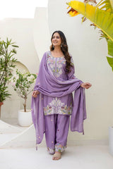 Woman in a purple traditional outfit with floral patterns in an outdoor setting.