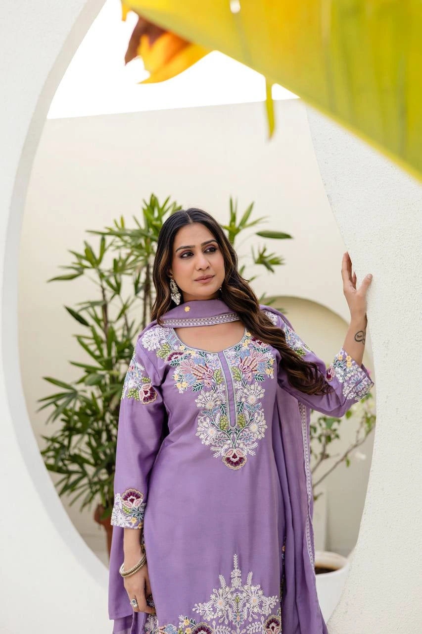 Woman in a purple embroidered outfit standing in front of a circular mirror with plants in the background