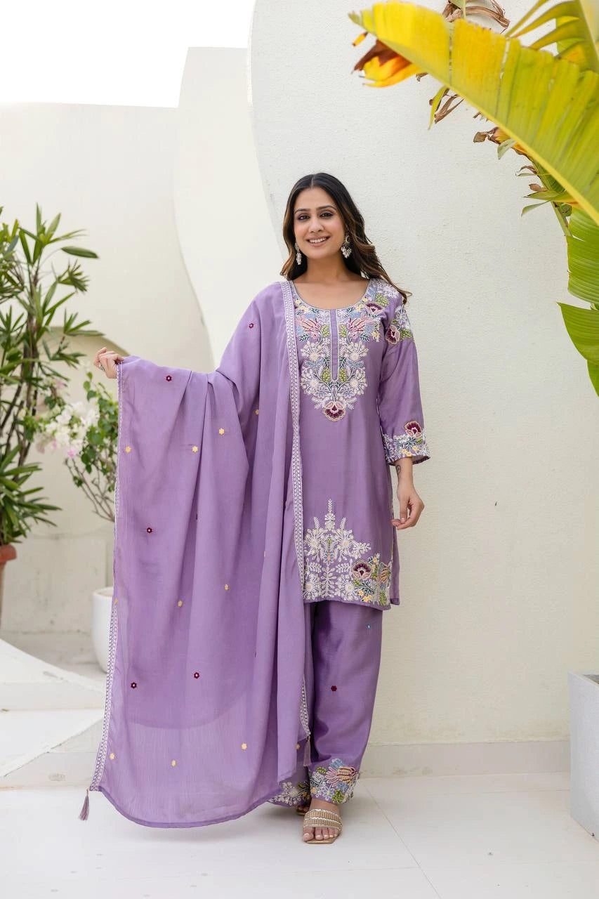 Woman wearing a purple traditional outfit with floral patterns in an indoor setting.