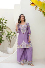 Woman wearing a purple embroidered outfit in a minimalistic setting with plants.