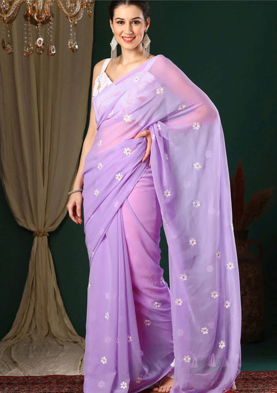 Woman wearing a lavender saree with white floral patterns against a dark background