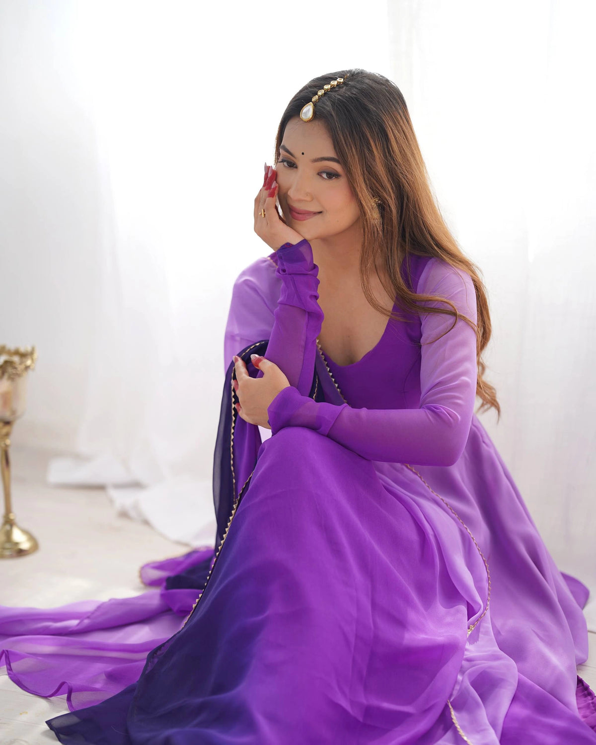 A rear view of a woman showing the deep back of her purple dress, which features a tie-up detail with tassels, as she looks back over her shoulder.