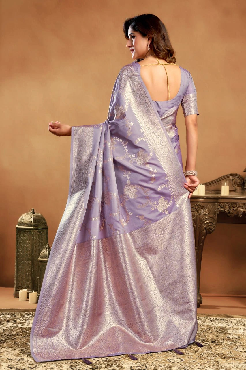 Woman wearing a light purple saree with a patterned design, standing against a beige background.