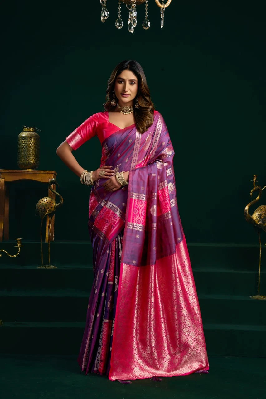 Woman in a pink and purple saree standing against a dark green background