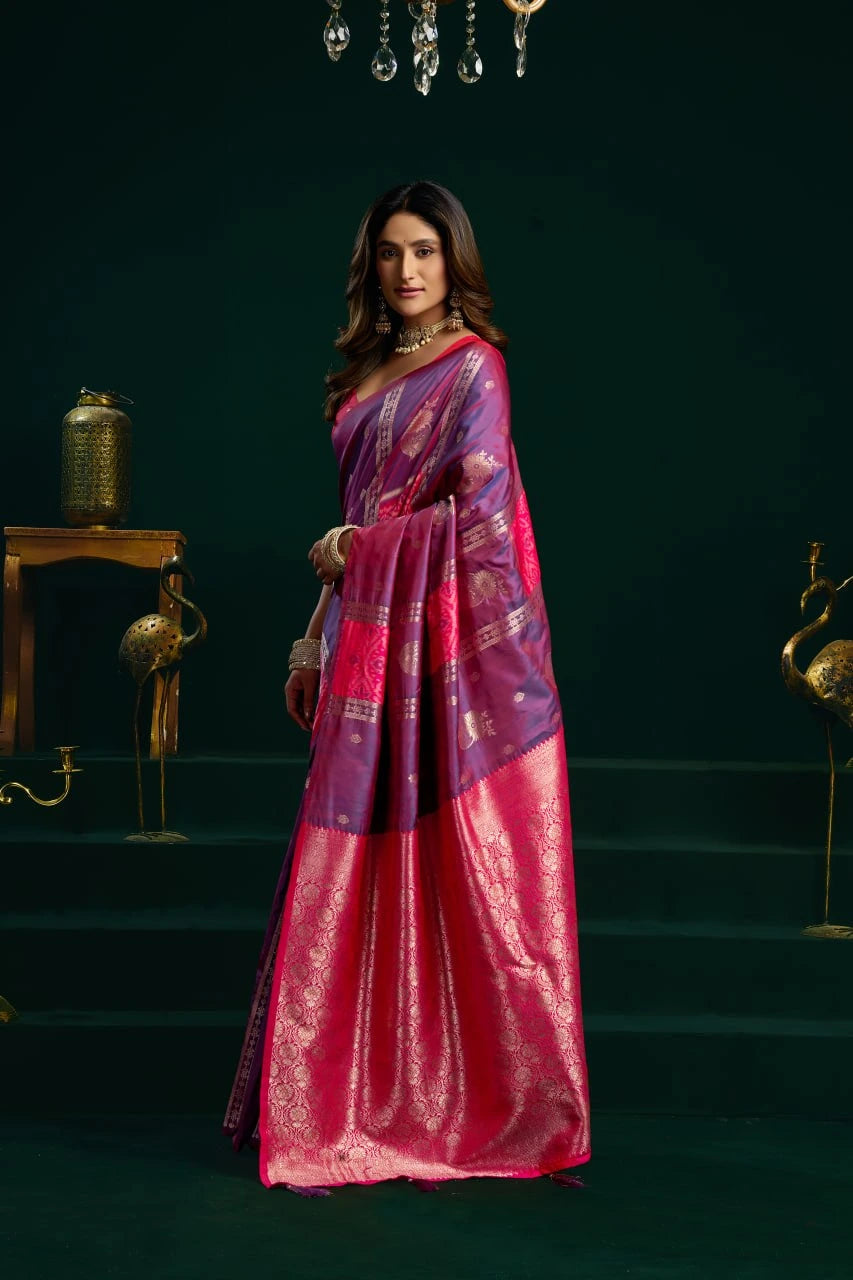 Woman wearing a pink and purple saree in a dark room with decorative elements.