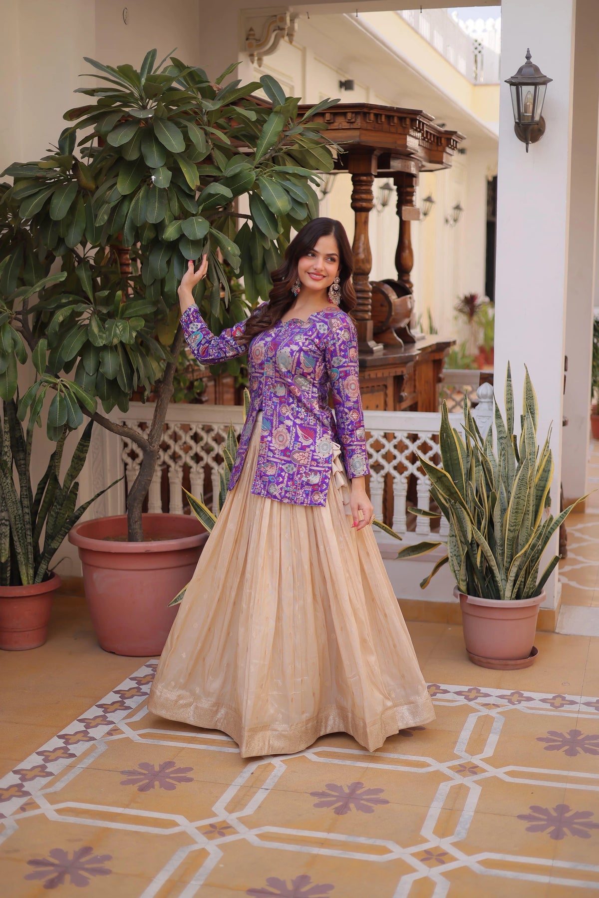 Woman in a purple top and beige skirt standing in a decorated indoor setting with plants.