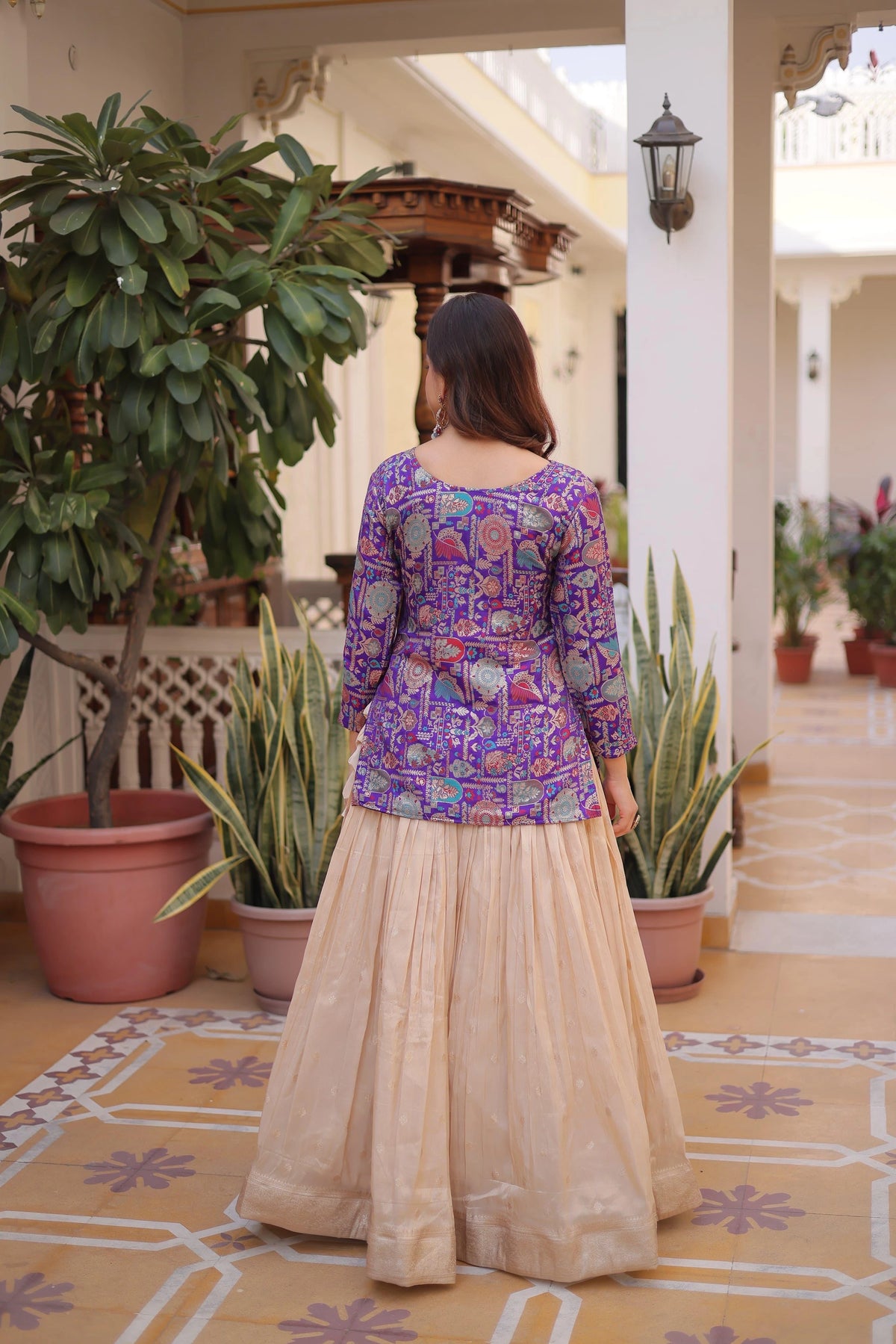 Woman in a colorful traditional outfit standing in a decorated indoor setting with plants.
