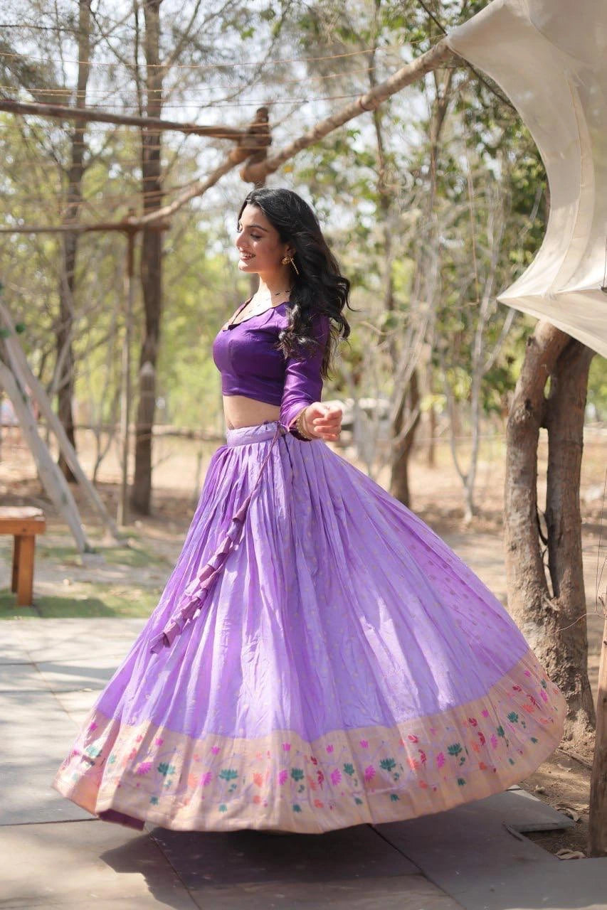 Woman in a purple traditional outfit standing outdoors with trees in the background