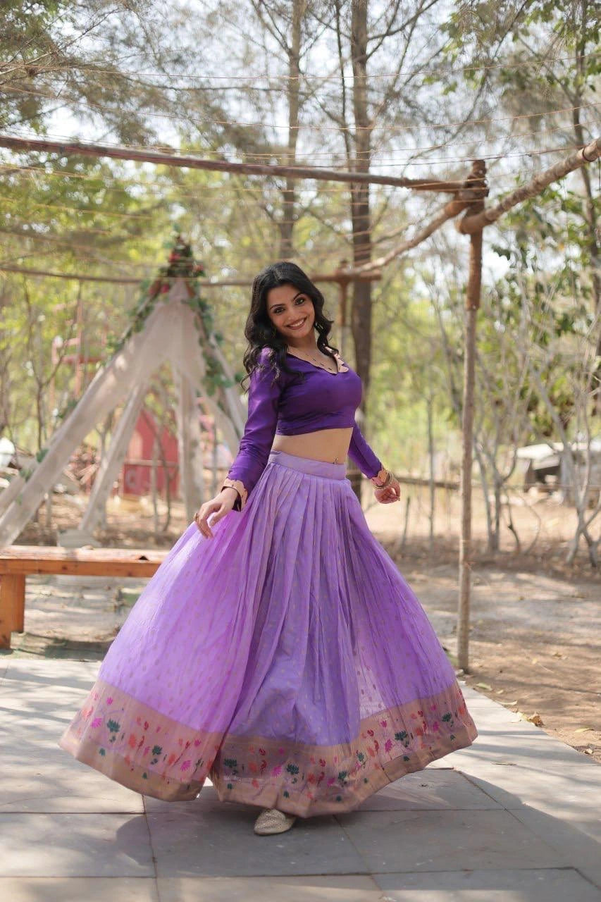 Woman in a purple traditional outfit standing outdoors with trees in the background