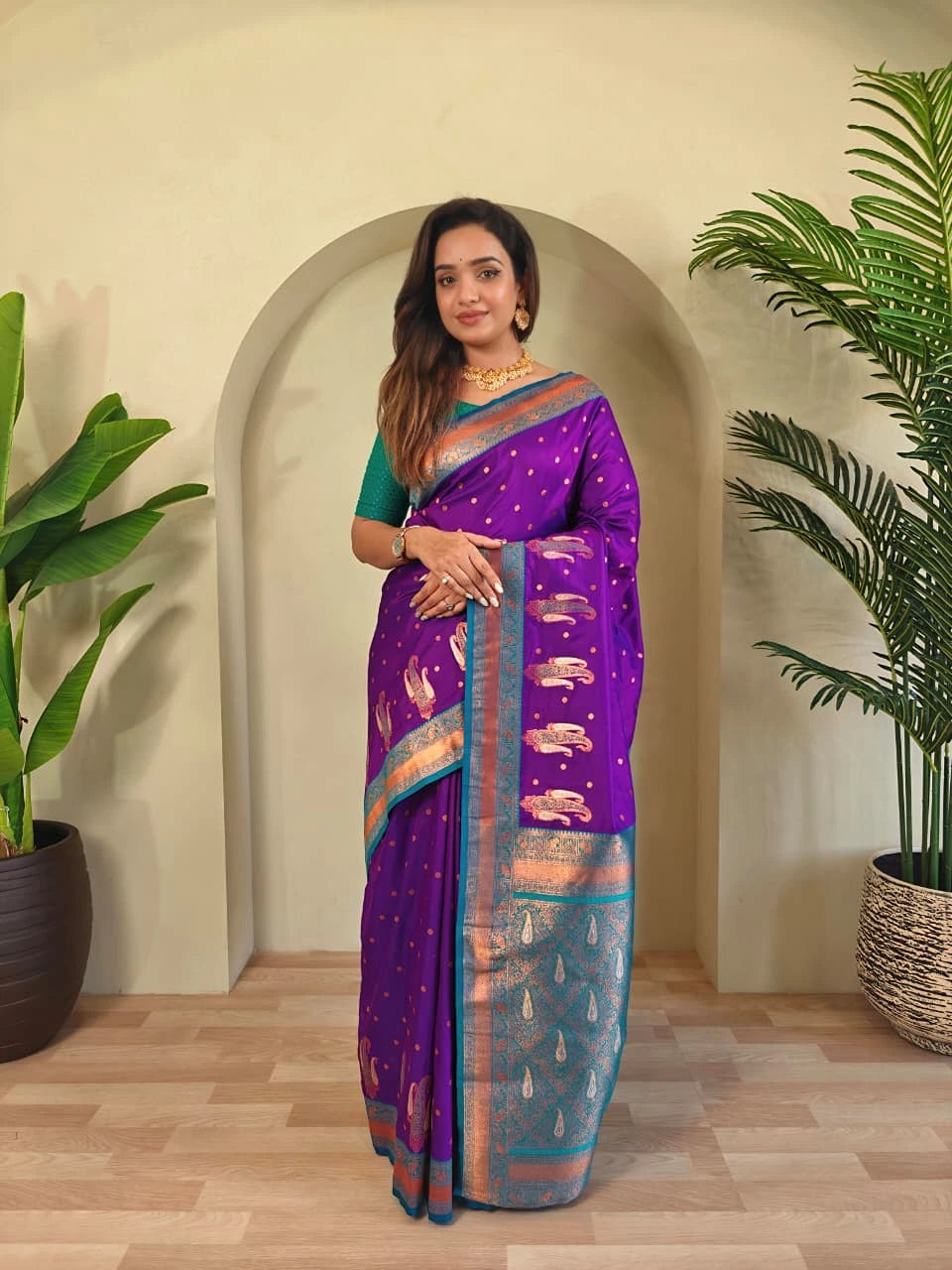 Woman wearing a purple saree with a green background and plants on either side.