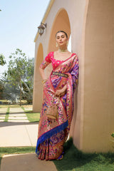 Woman in a colorful saree standing outdoors near a building with greenery.