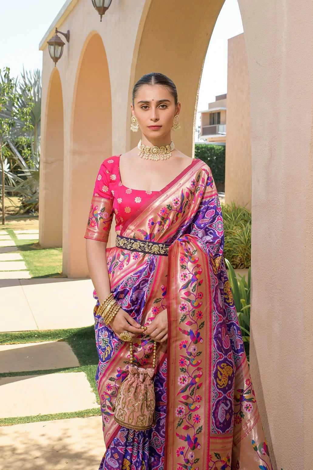 Woman in a colorful saree standing outdoors near architectural elements.