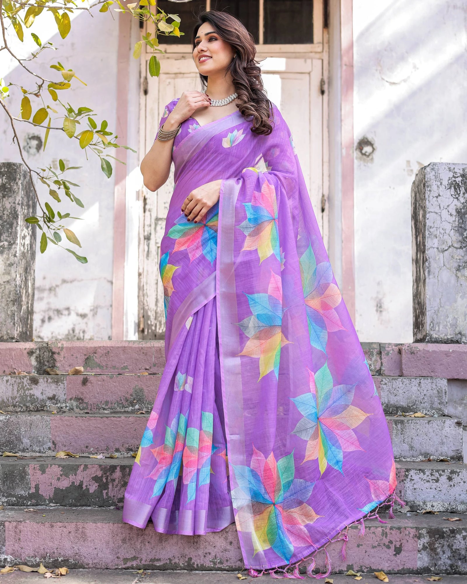 Woman wearing a purple saree with colorful patterns standing outdoors.