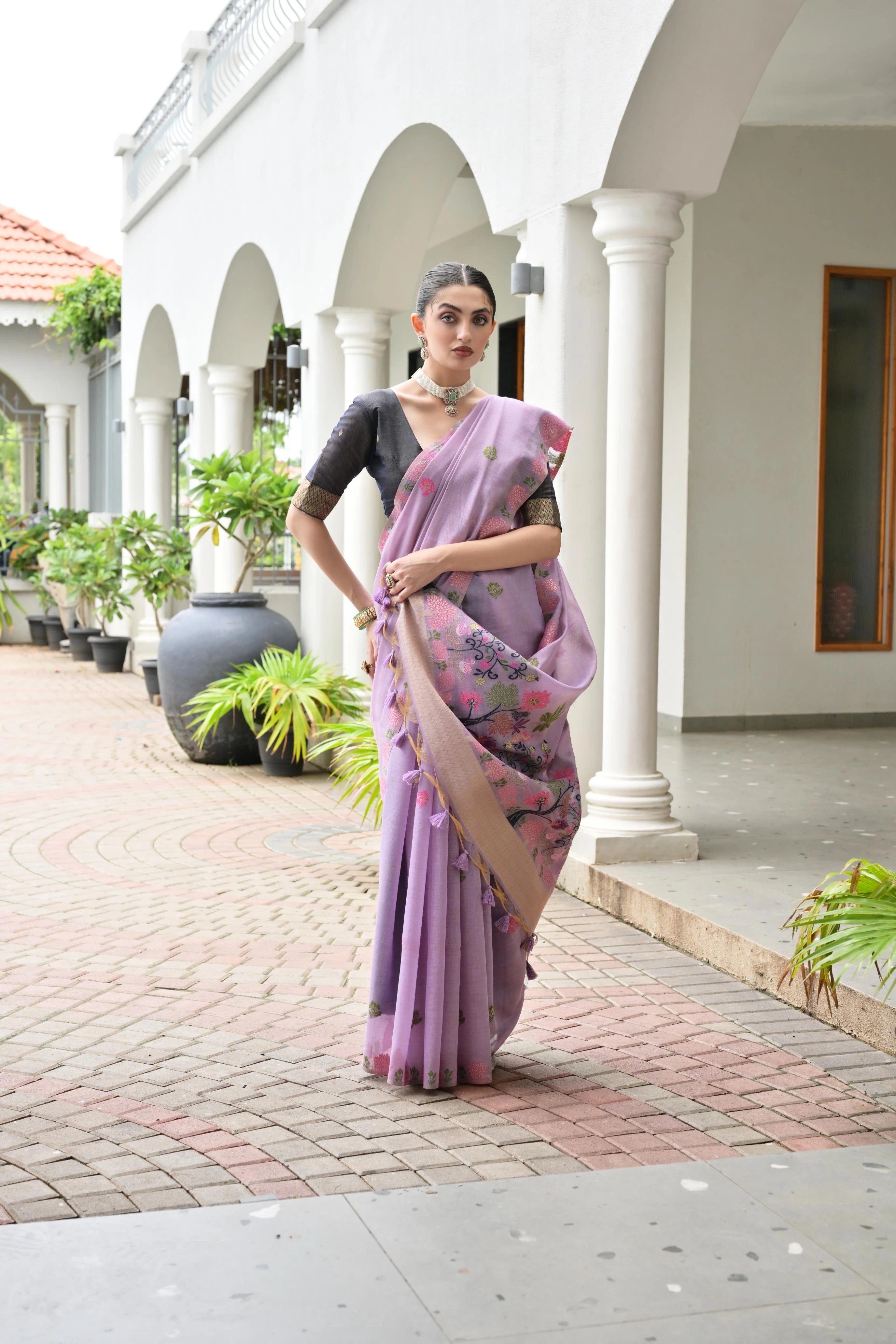 Woman in a purple saree standing in front of a white building with columns.
