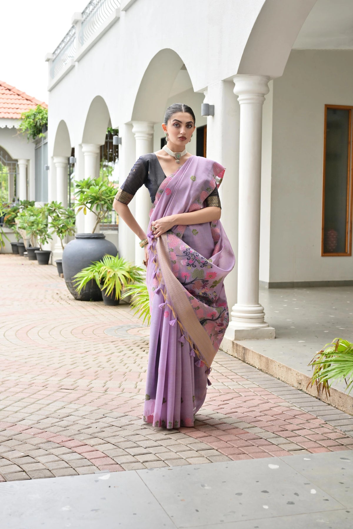 Woman in a purple saree standing in front of a white building with columns.