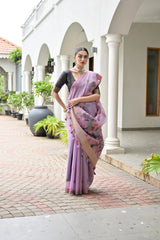 Woman in a purple saree standing in front of a white building with columns.