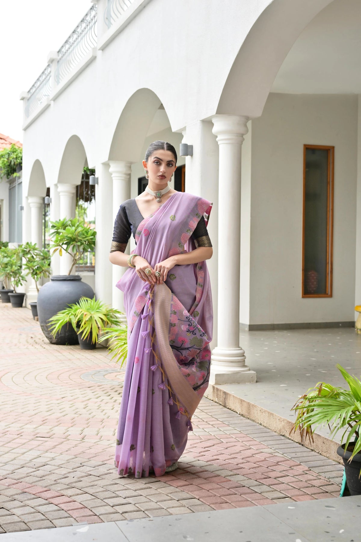 Woman in a lavender saree standing in front of a white building with arches.