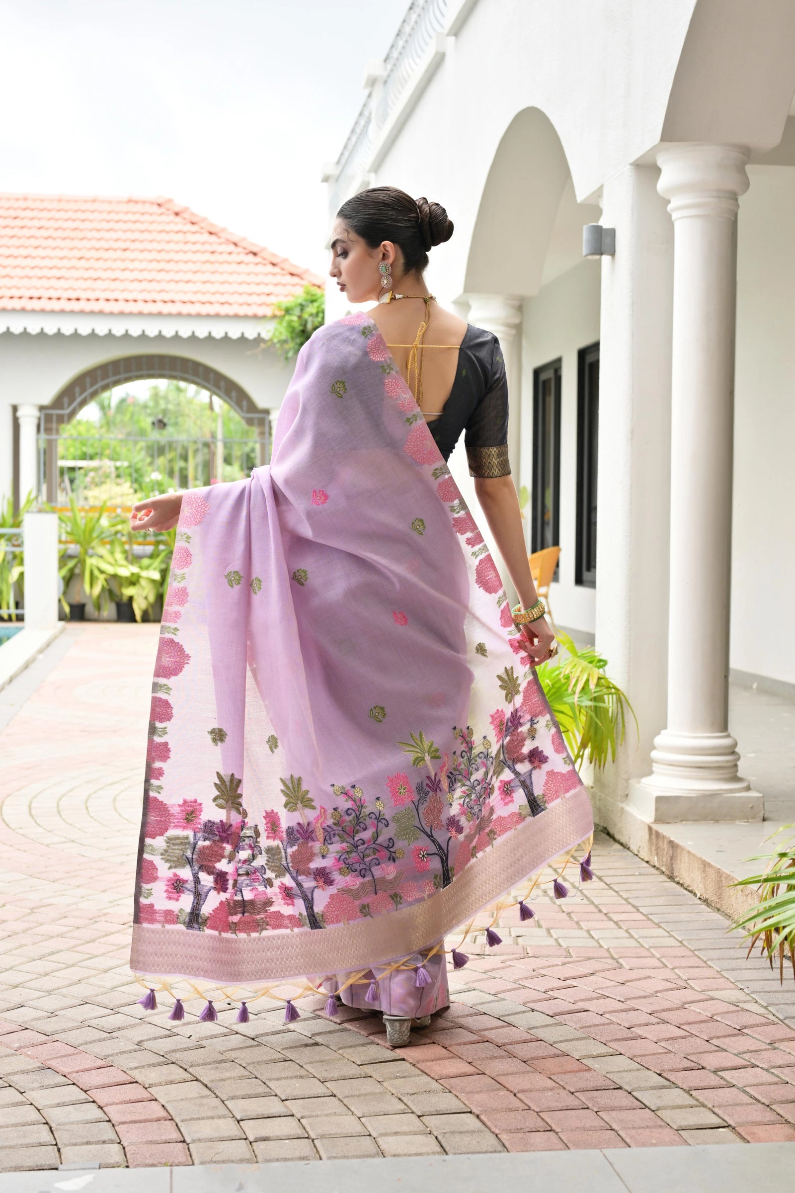 Woman wearing a pink saree with floral patterns in an outdoor setting.