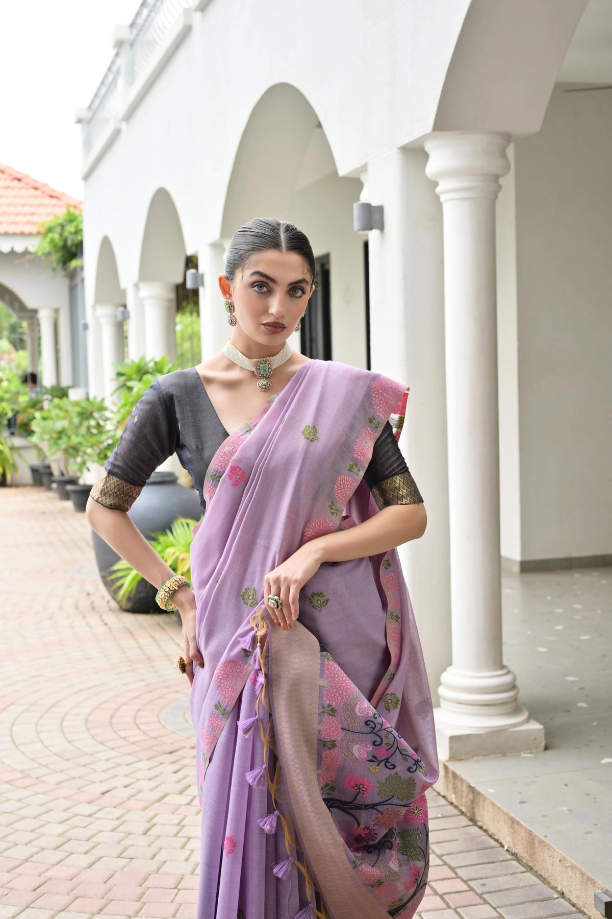 Woman in a purple saree with floral patterns standing in front of a white building.