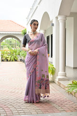 Woman in a lavender saree with floral patterns standing in front of a white building.