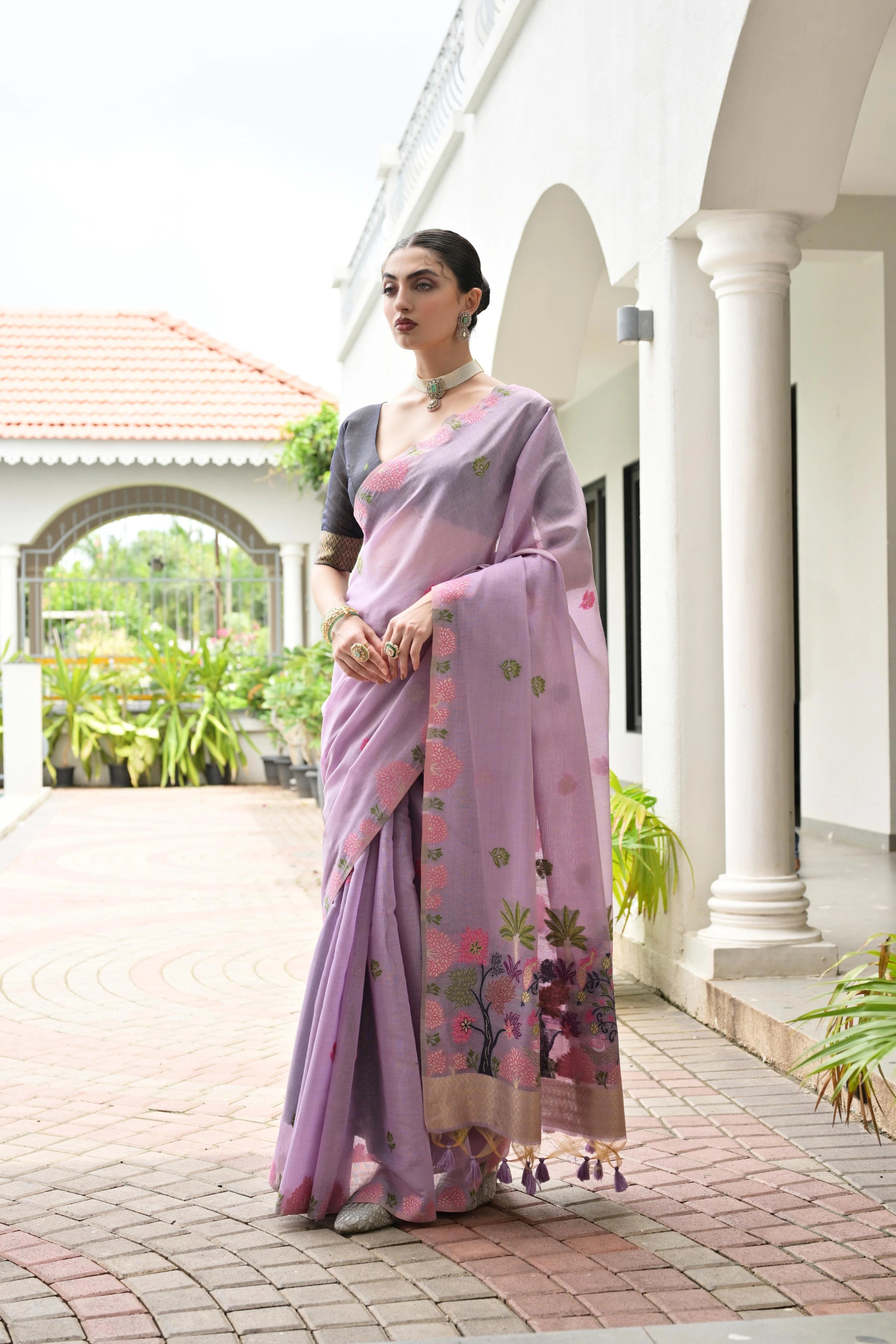 Woman in a pink saree with floral patterns standing in front of a white building.