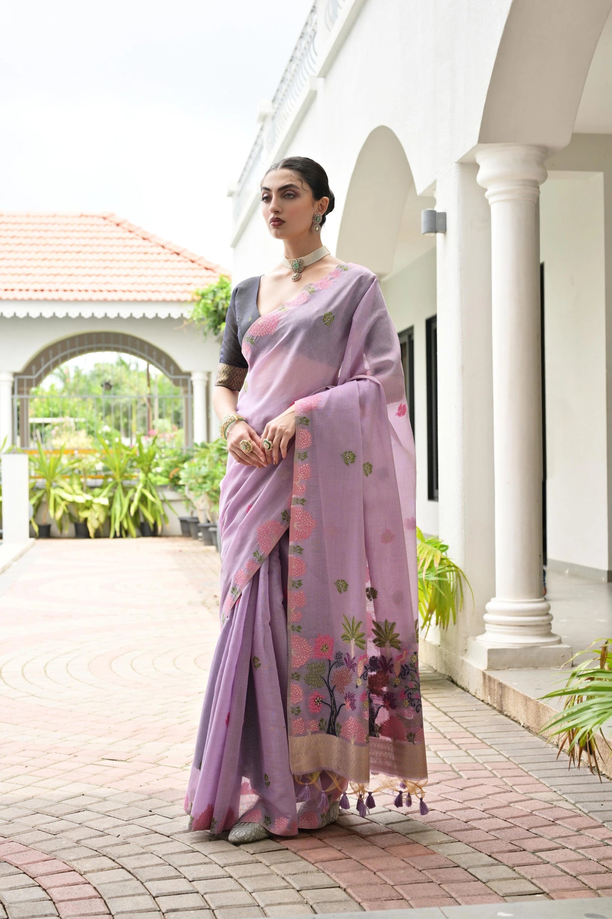 Woman in a pink saree with floral patterns standing in front of a white building.