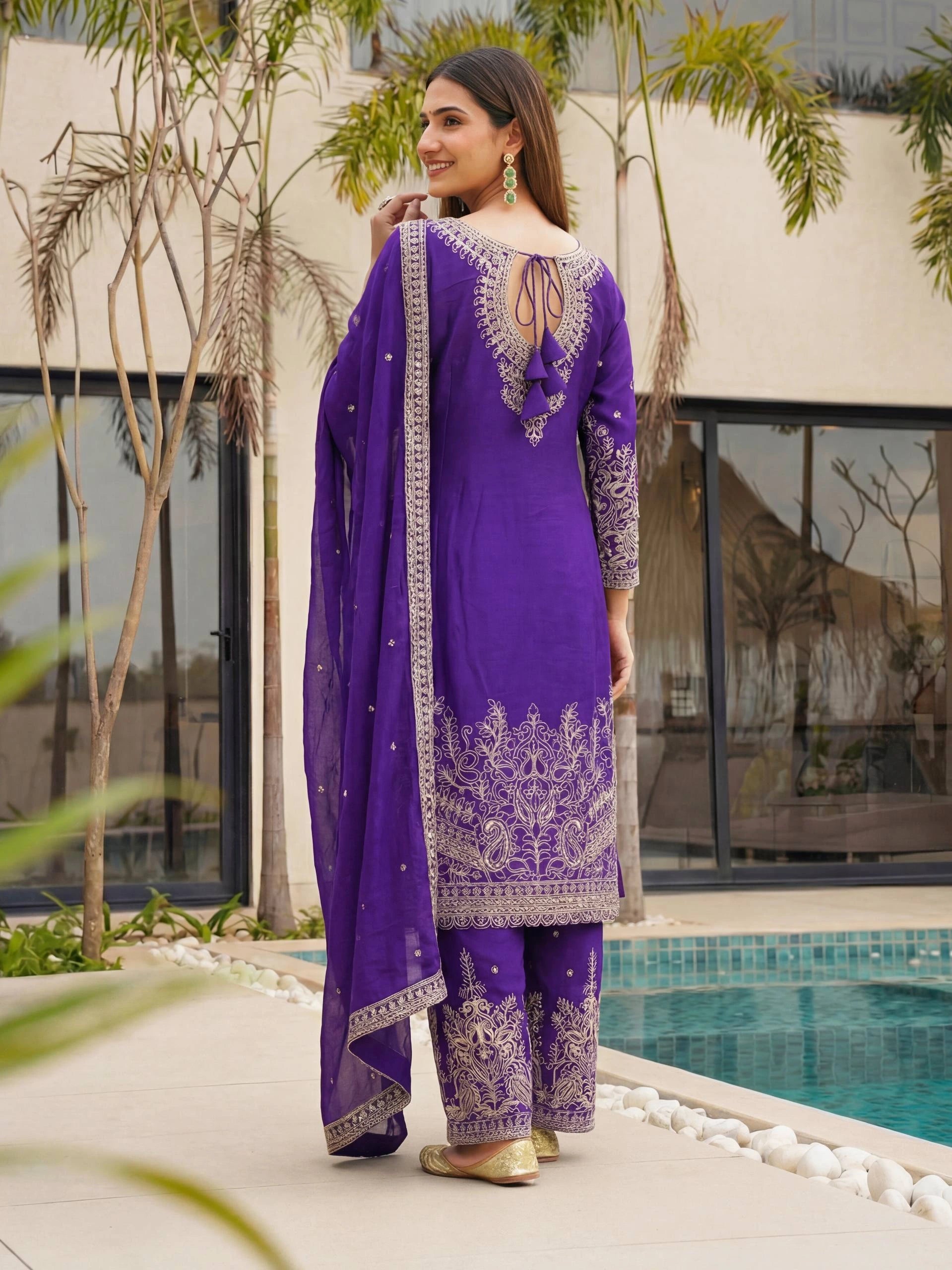 Woman in a purple traditional outfit standing by a pool with greenery around.
