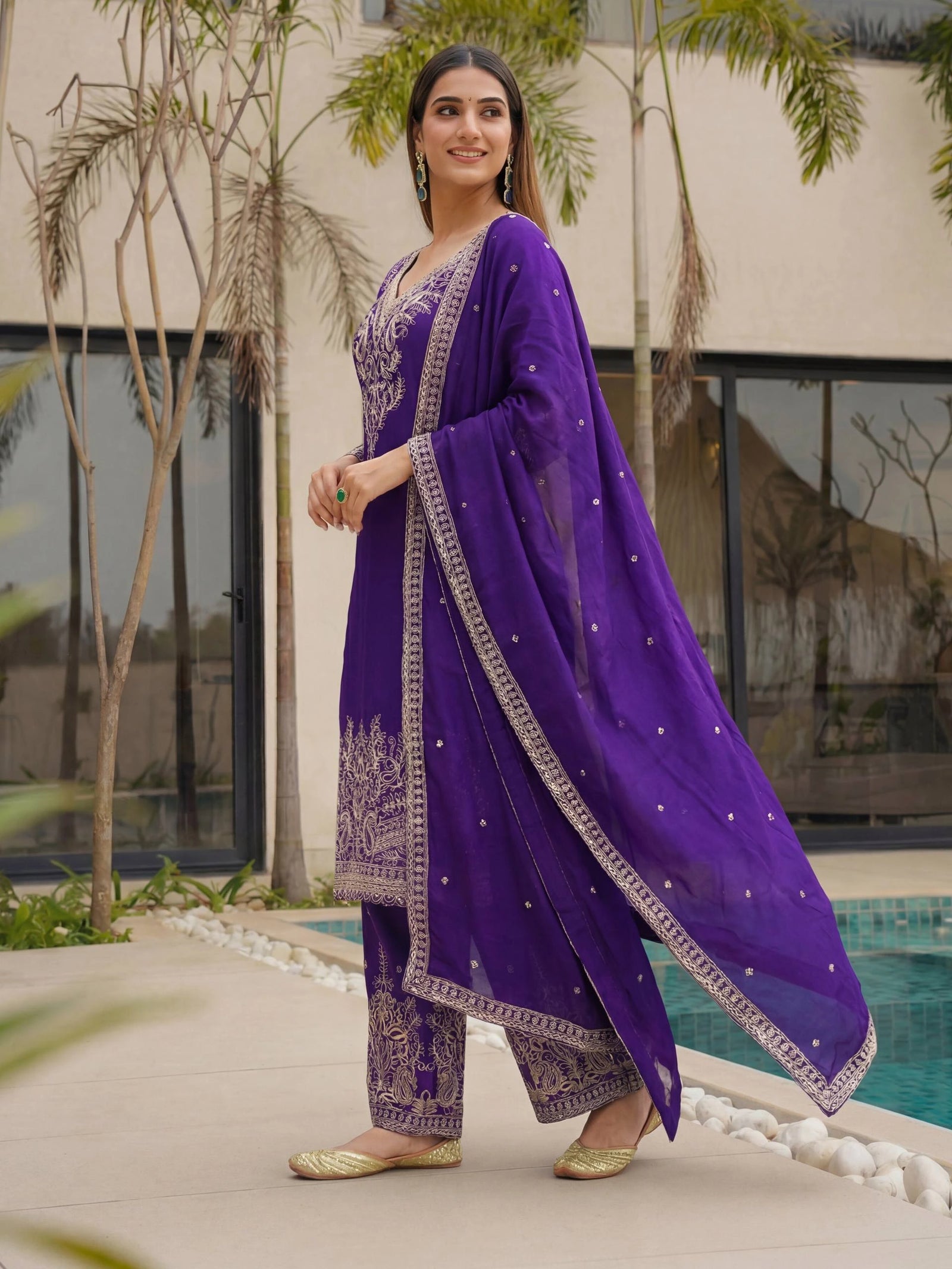 Woman in a purple traditional outfit standing by a pool with greenery around.