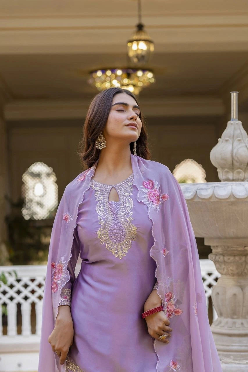 Woman in a lavender traditional outfit with floral embroidery in an elegant indoor setting.